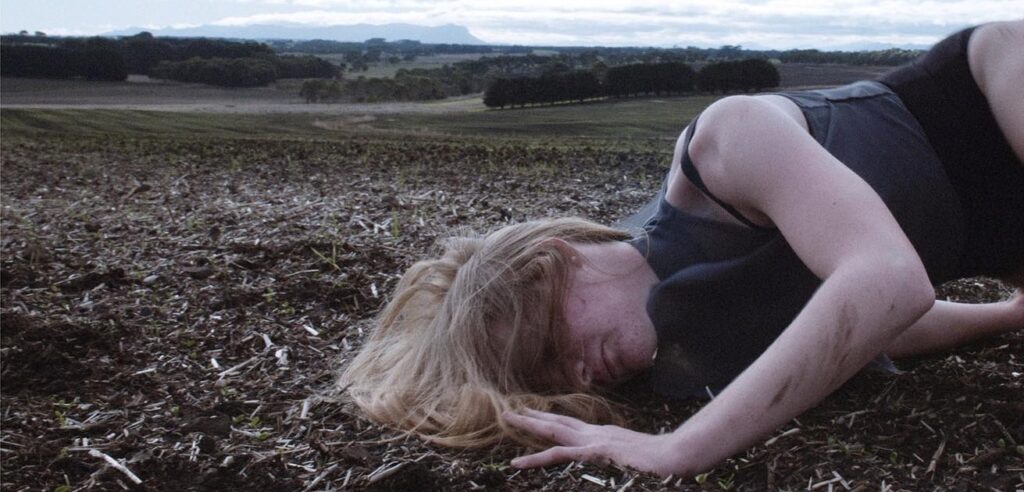 Women with blonde hair laying in dirt in a field.