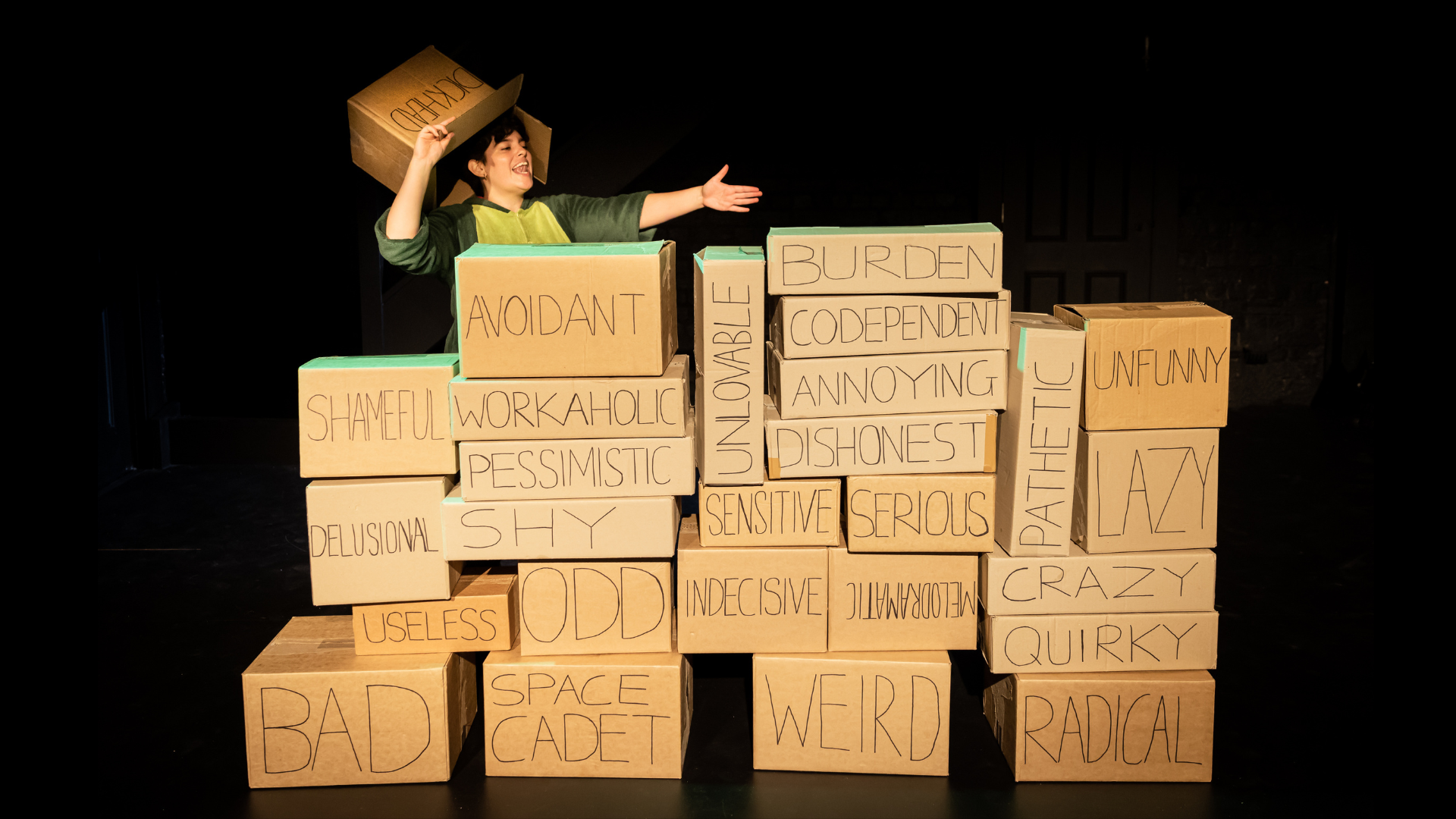 Person standing behind a wall of cardboard boxes with negative words written on them.