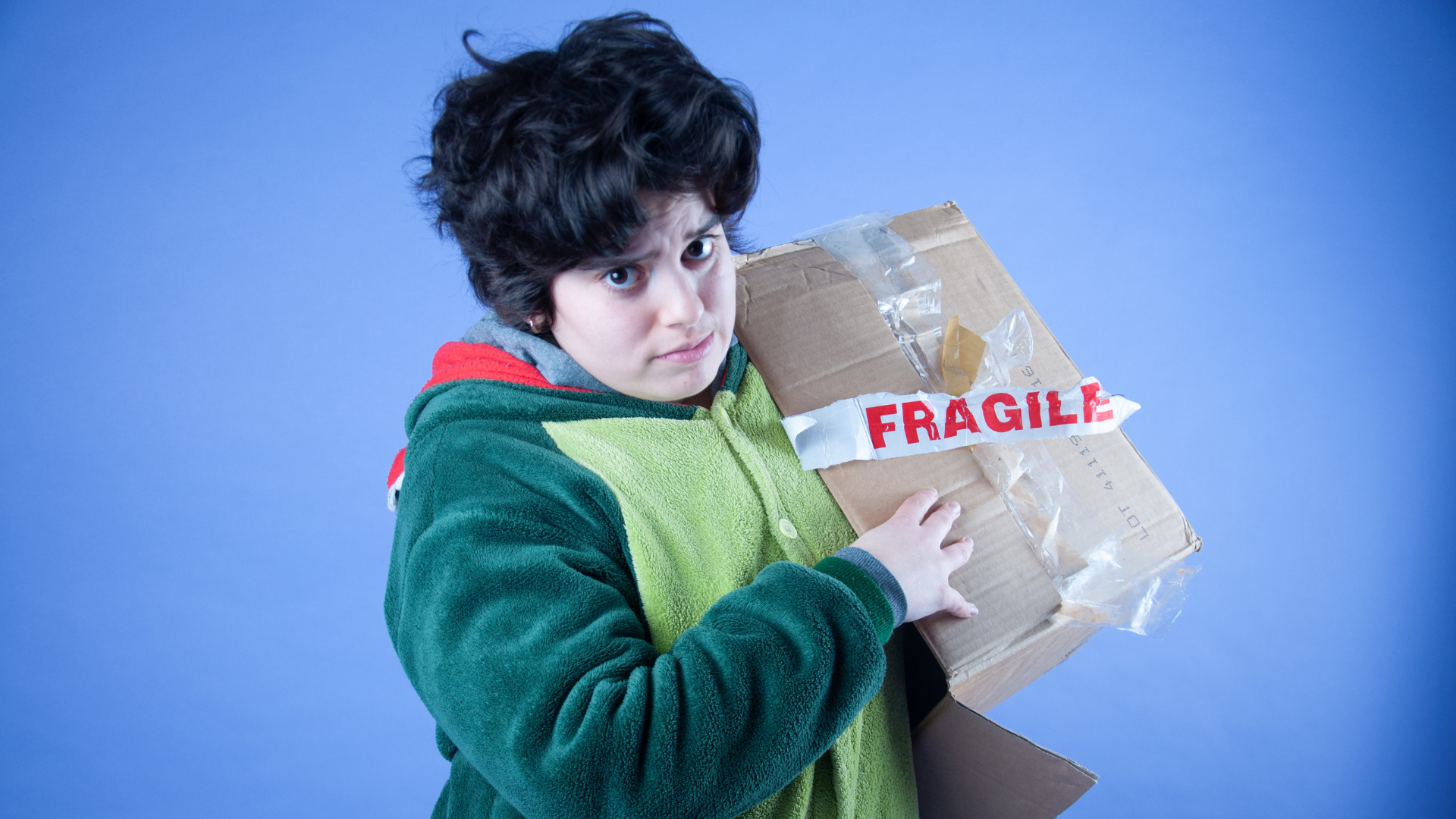 Person in a green onesie holding a carboard box with a fragile sticker on it.