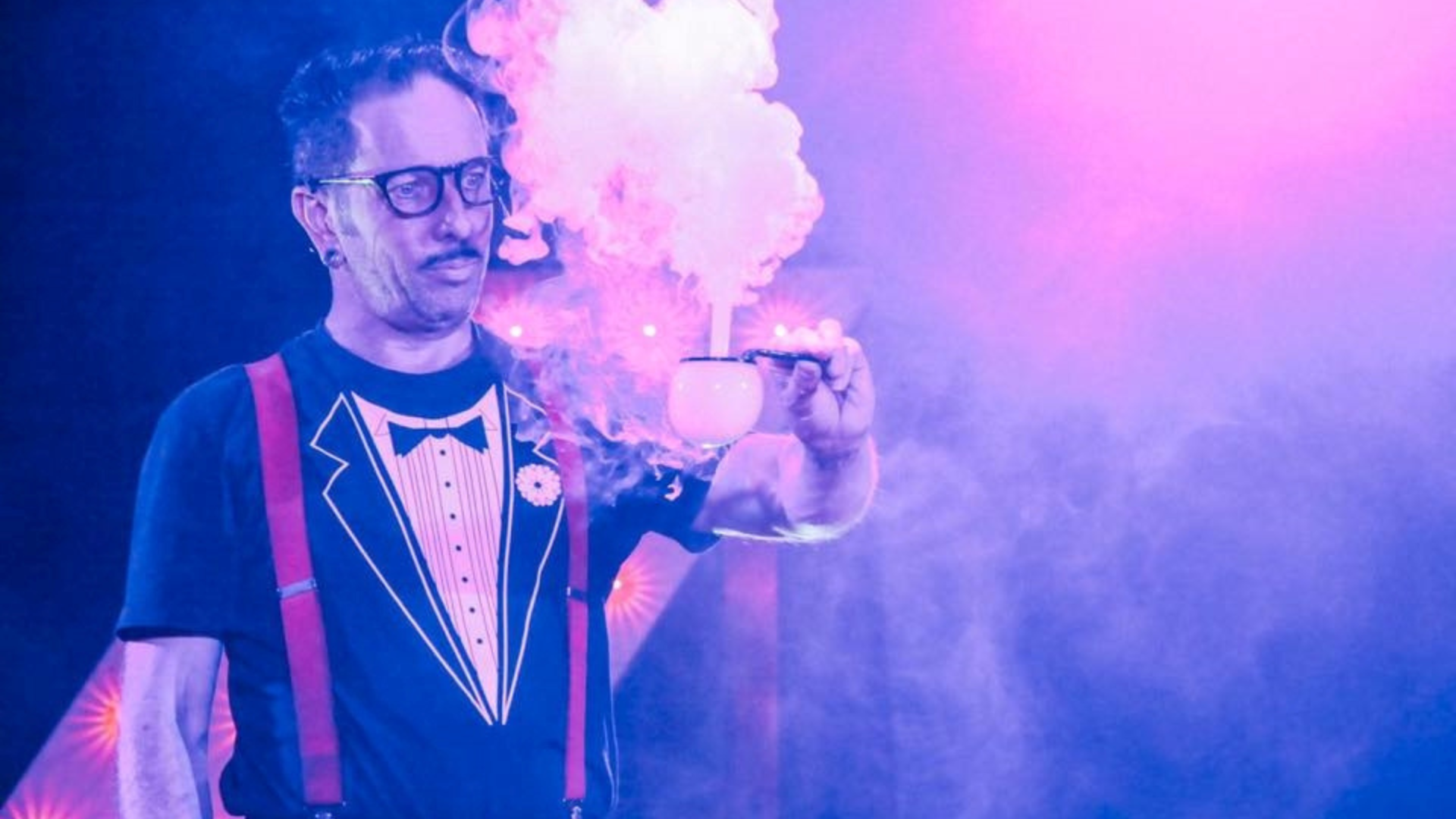 Man in black shirt and red suspenders holding a bubble releasing smoke