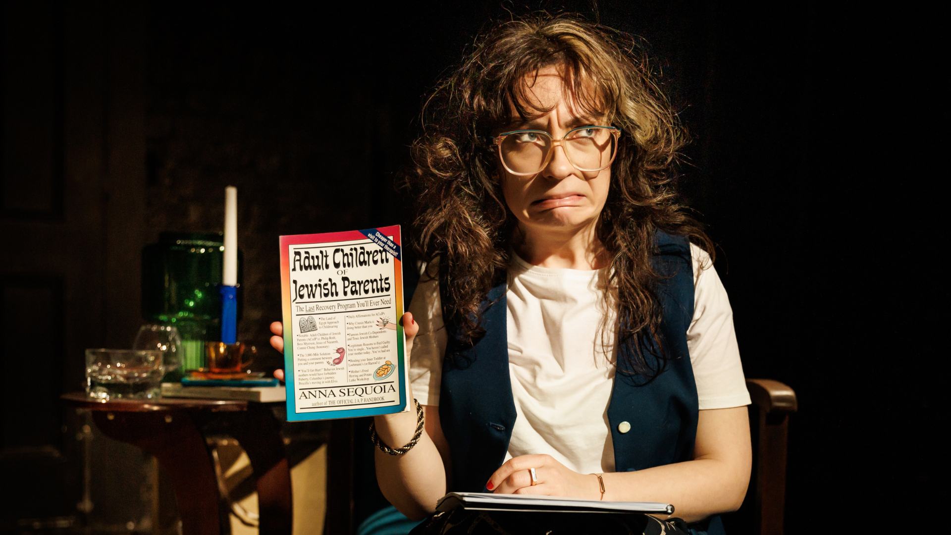 Woman with brown hair looking awkward holding a book titled 'Adult Children of Jewish Parents'