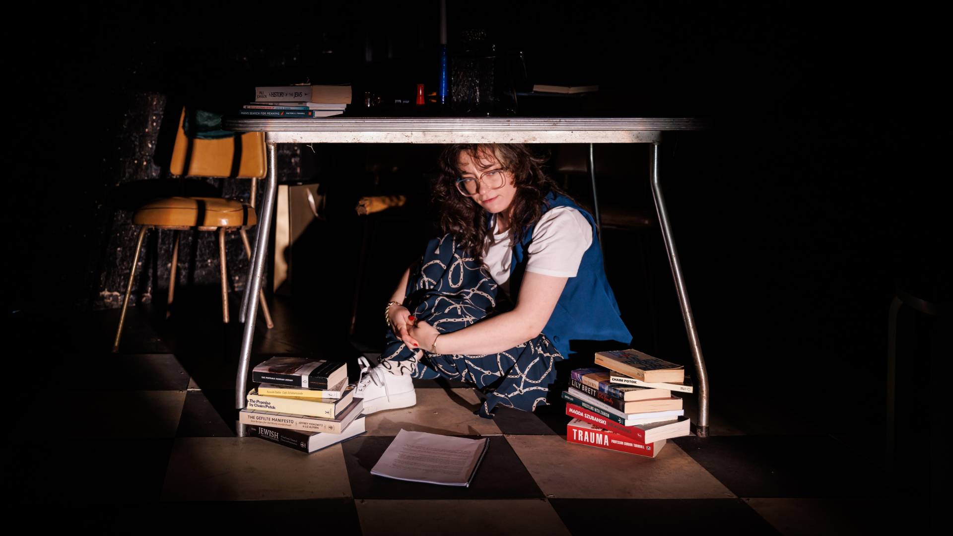 Woman sitting under a table surrounded by books