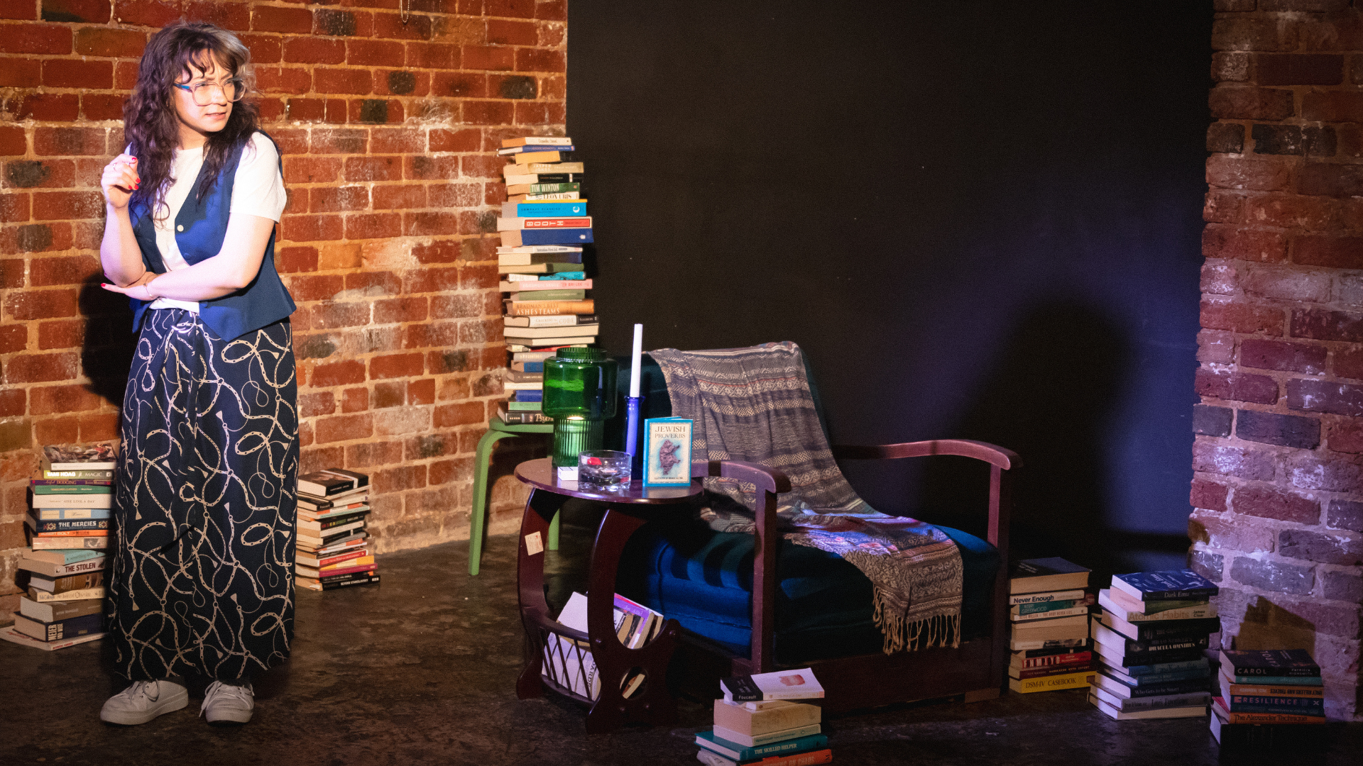 Woman standing on a stage by a chair and piles of books